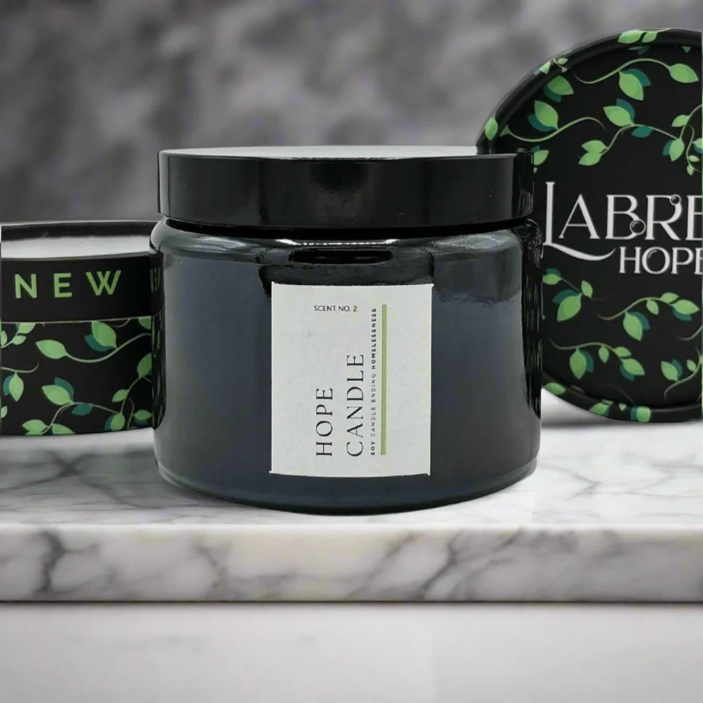 A black glass candle jar with a black lid. The candle is placed on a white marble surface