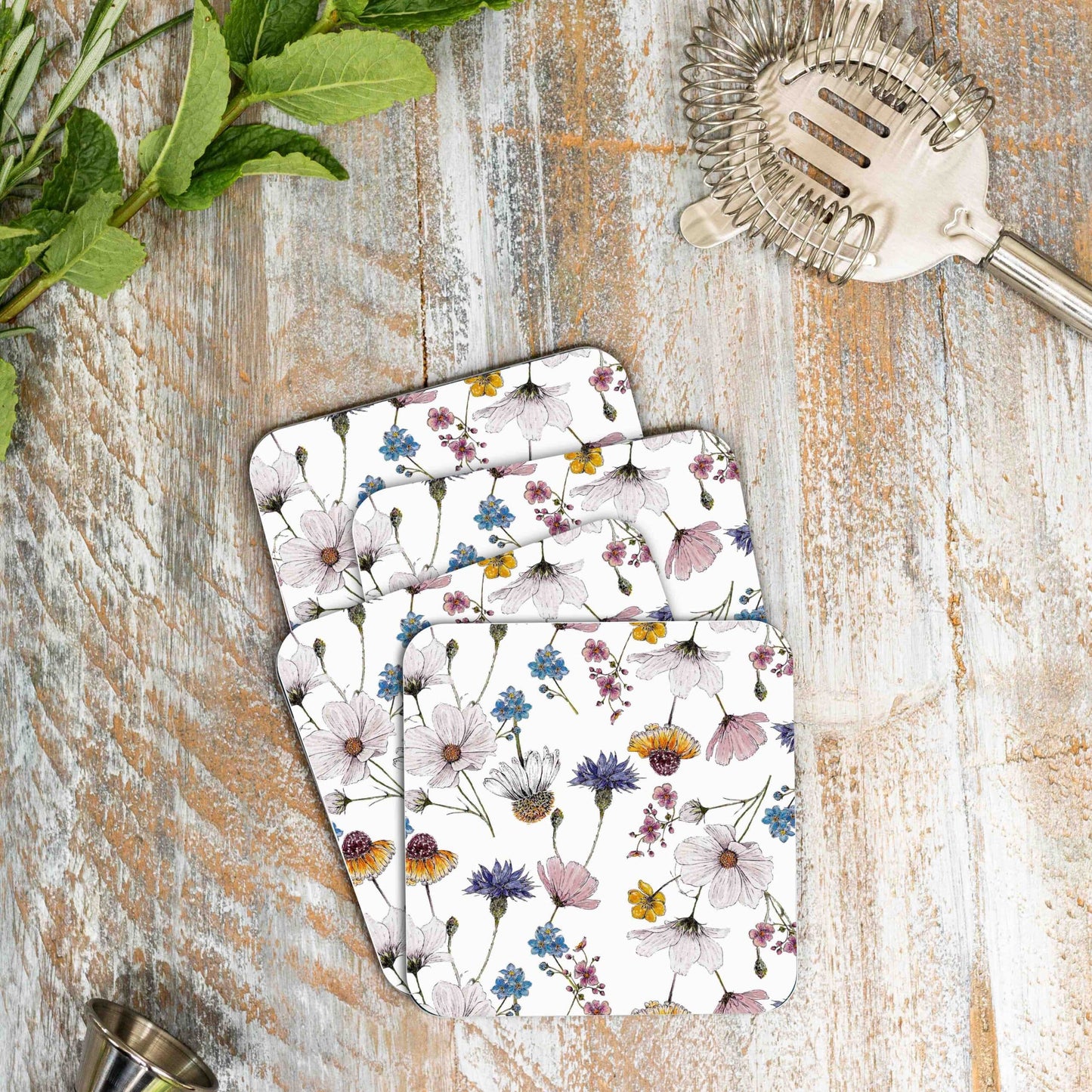 Lifestyle photo of four coasters in a spreading stack on a wooden surface. The coasters have a repeating watercolour motif of flowers.