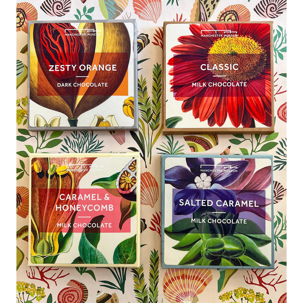 This image shows four colourful boxes of chocolate bars with different flavours. Presented on a floral print backdrop.