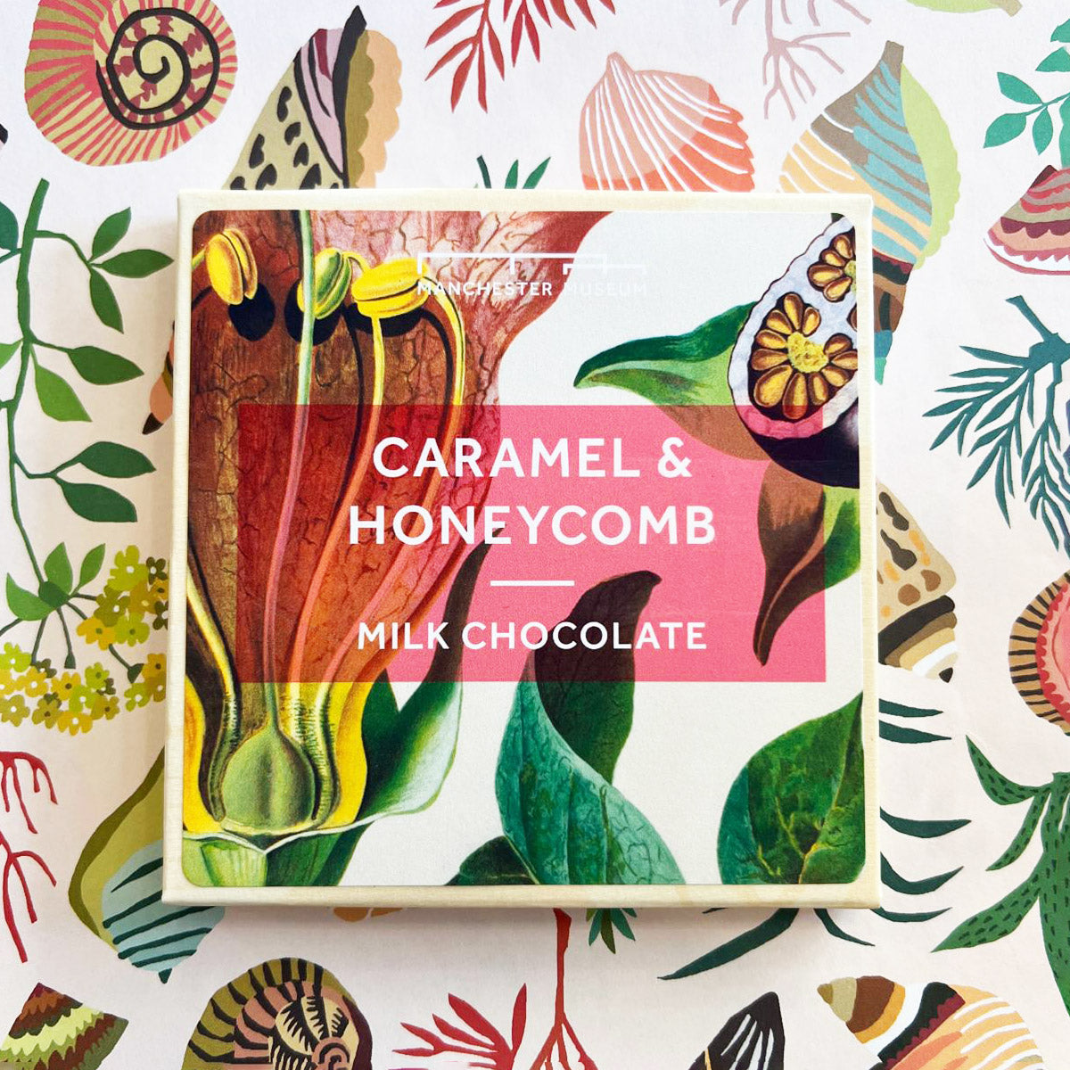 Packaging for caramel chocolate featuring a Manchester Museum botanical print on the cover. Presented on a white floral backdrop.