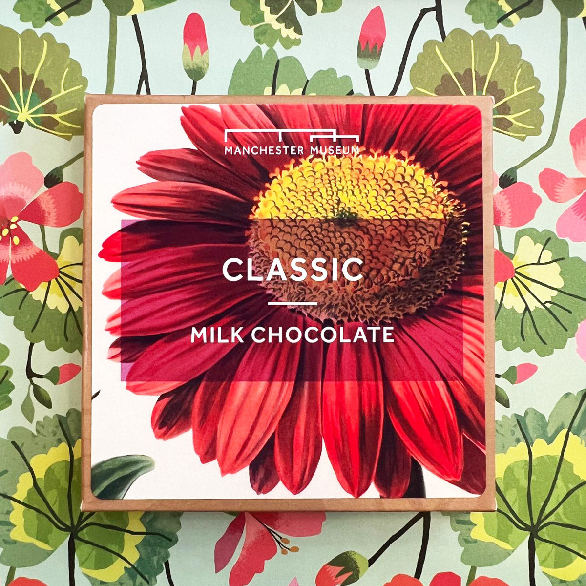 Classic milk chocolate squared packaging with large print of a close up of a red flower. Presented on a green and pink and green floral background