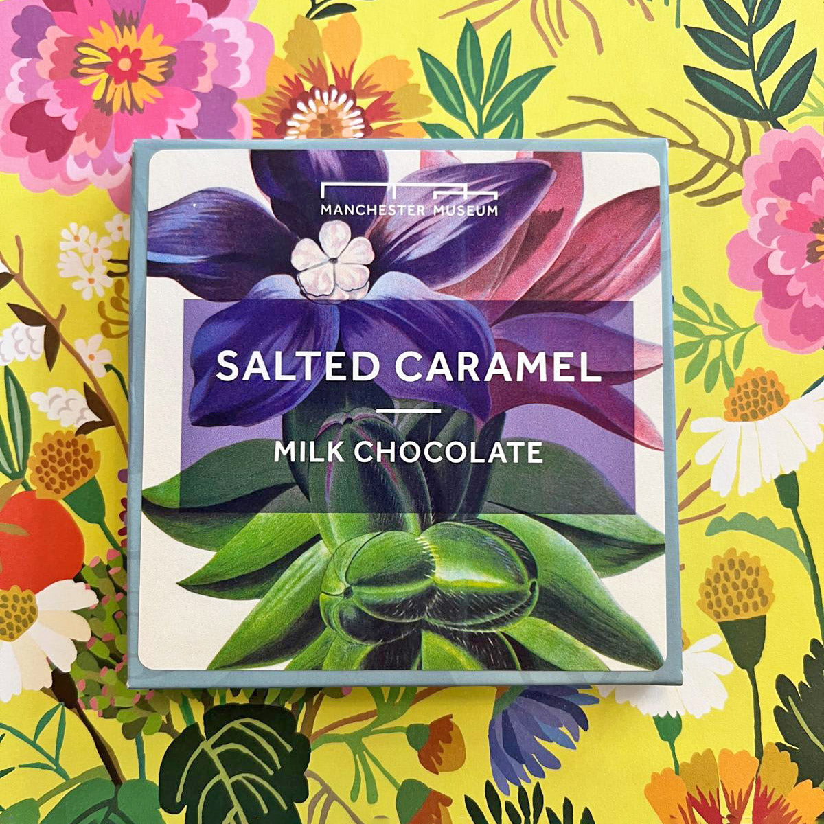 Square packaging for salted caramel chocolate featuring a Manchester Museum botanical print. Presented on a yellow floral backdrop.