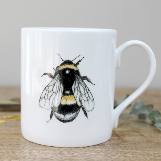 White mug with a picture of a bee on it. Photographed on a wooden surface.