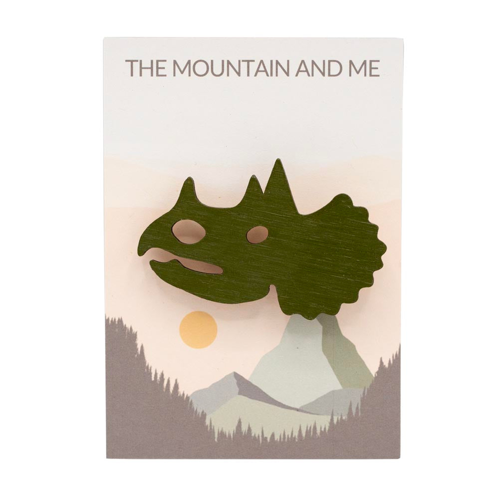 Wooden brooch shaped like a triceratops head on branded 'The Mountain and Me' backing card.