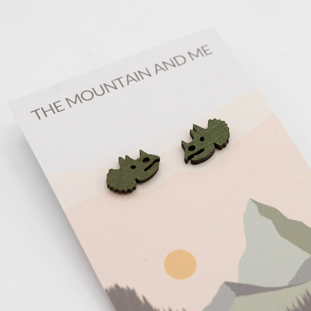 Wooden stud earrings in the shape of a Triceratops head, on branded backing card.
