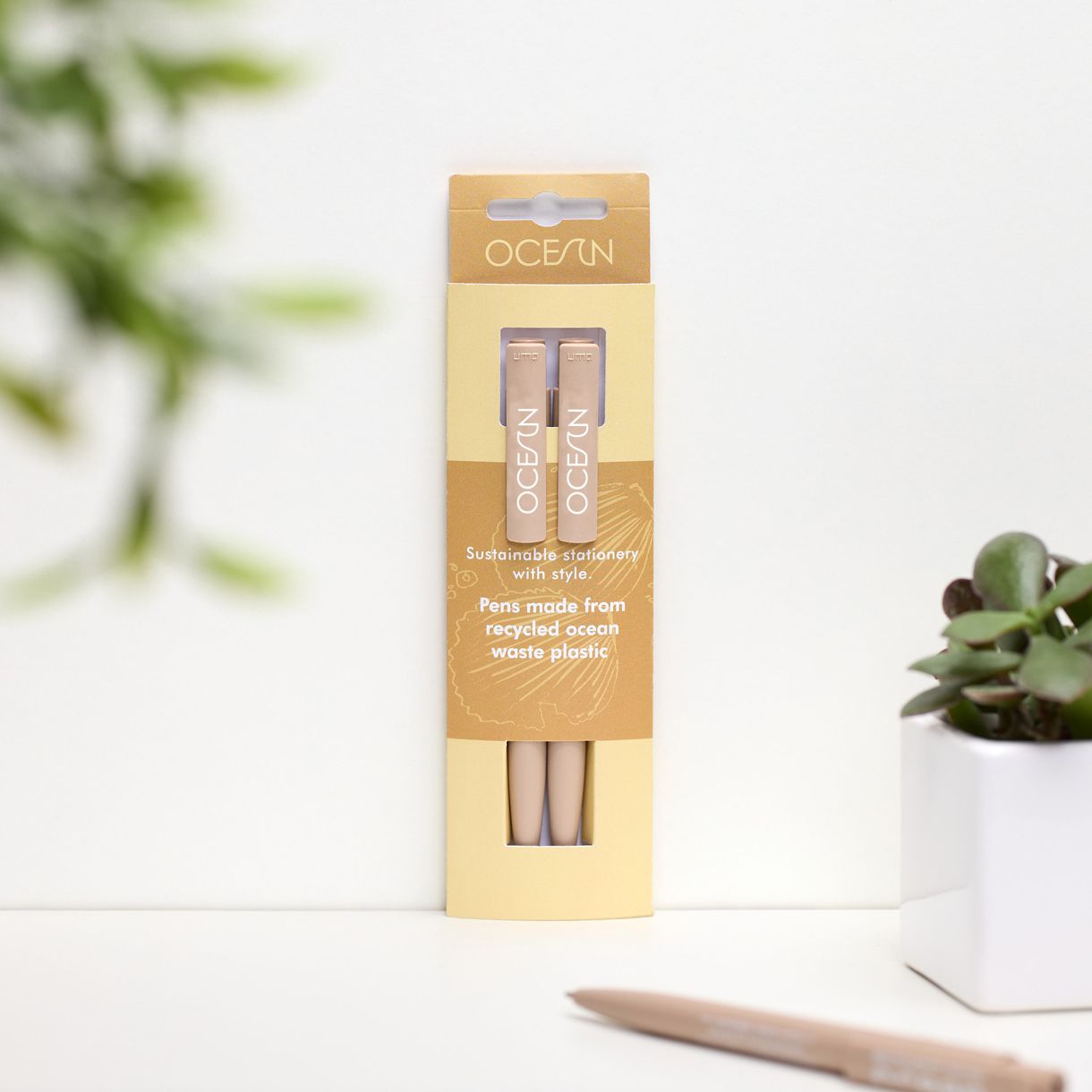 Lifestyle of a pack of two yellow pens with a third yellow pen in front of the pack and a small plant to the right.