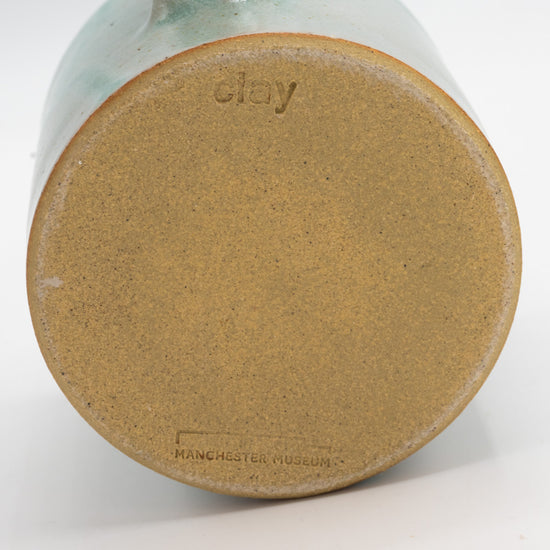Underneath of a mug with exposed clay. Clay studio logo is engraved at the top and Manchester Museum logo is engraved on the bottom.
