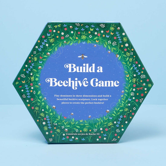 The hexagonal game box which has grass and flowers around the edges and a blue centre with white text: Build a Beehive Game.