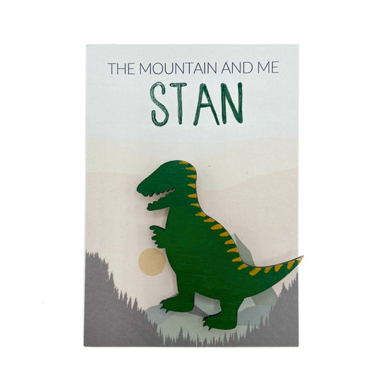 Green dinosaur broach against backing card with The Mountain and Me. White background.