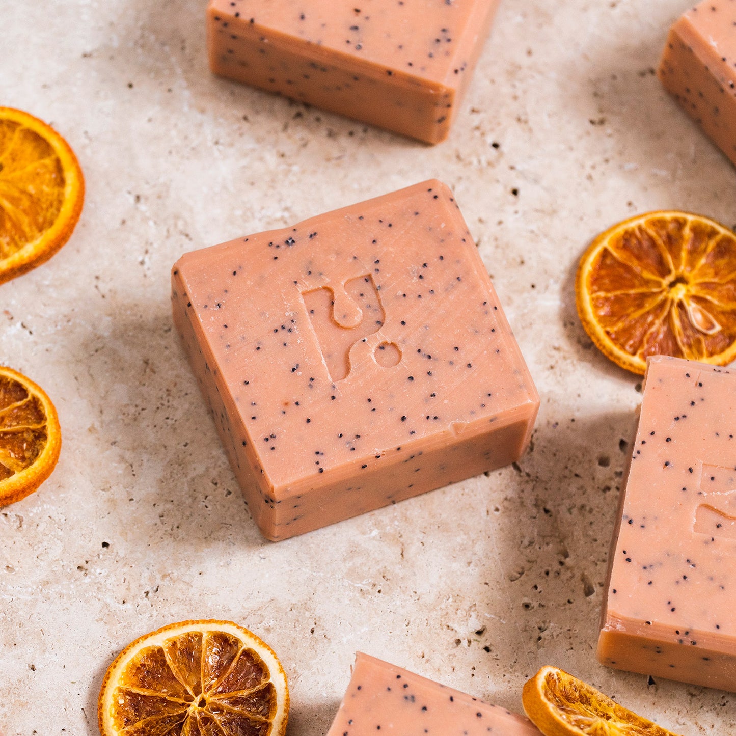 Pink speckled soap bar on a marbles surface with orange seeds around it.