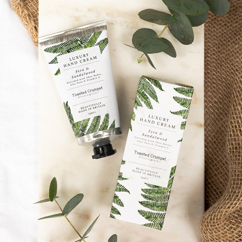 Hand cream and its packaging side by side on a marble surface with flora surrounding it
