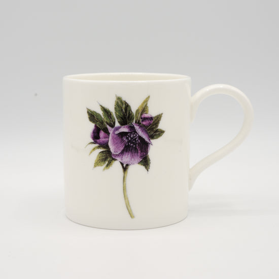 White mug with an illustration of a hellebore flower on it. Photographed against a white background.