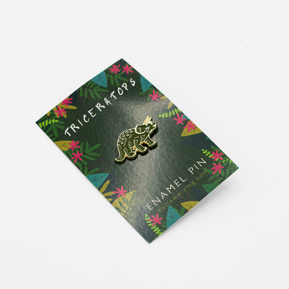 Enamel pin of a triceratops on a decorative card with colorful patterns