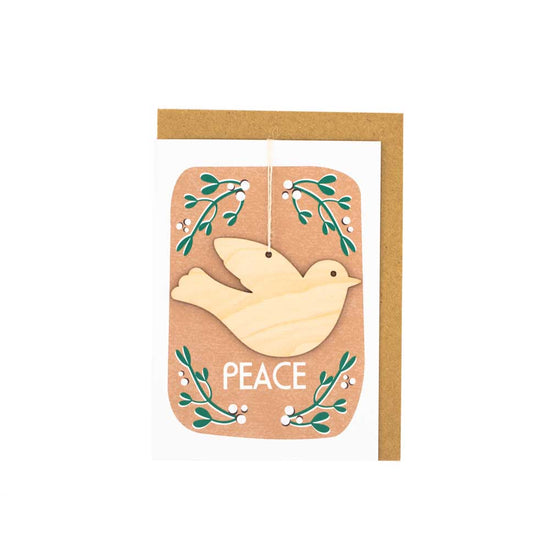 Card with brown envelope tucked inside, white background. Wooden dove decoration with the word 'Peace' underneath. Mistletoe border.