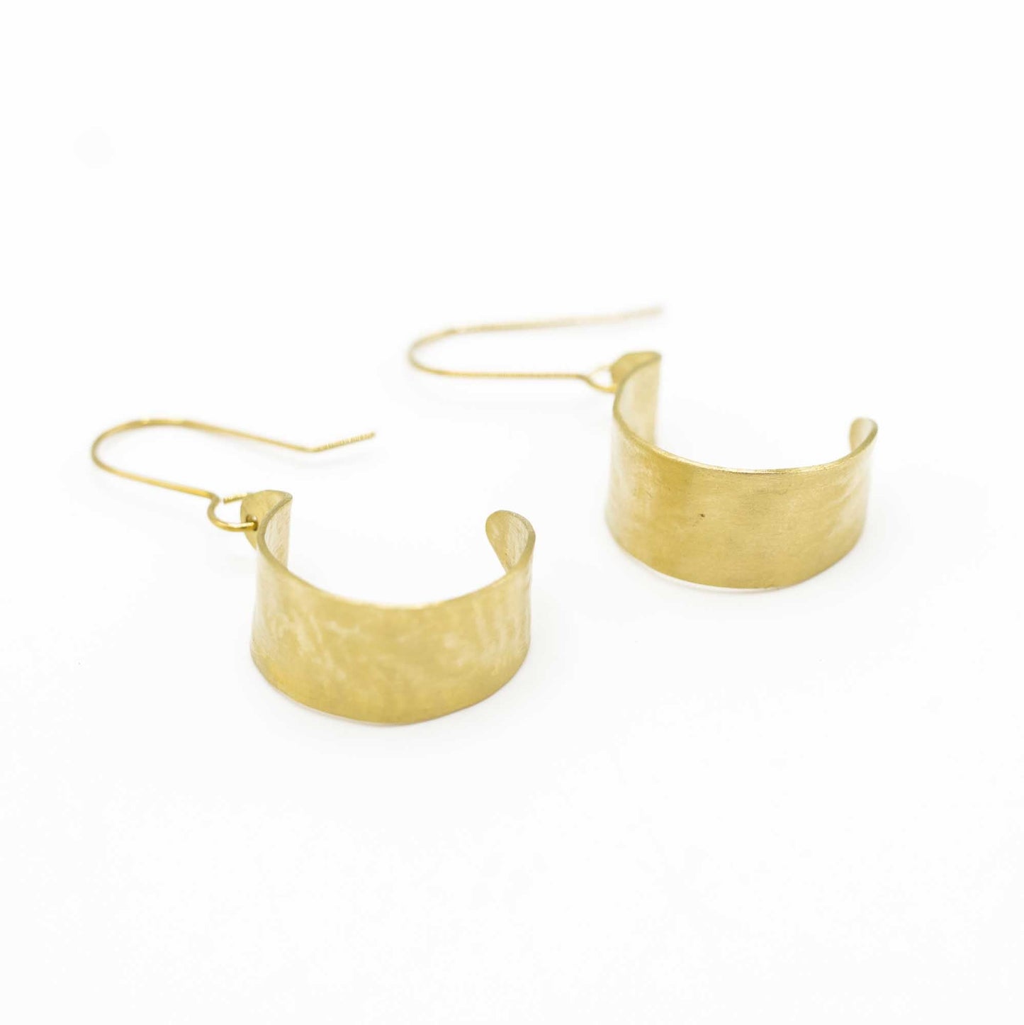 Hammered brass half-hoop earings lying on the side with the hoop towards the spectator.