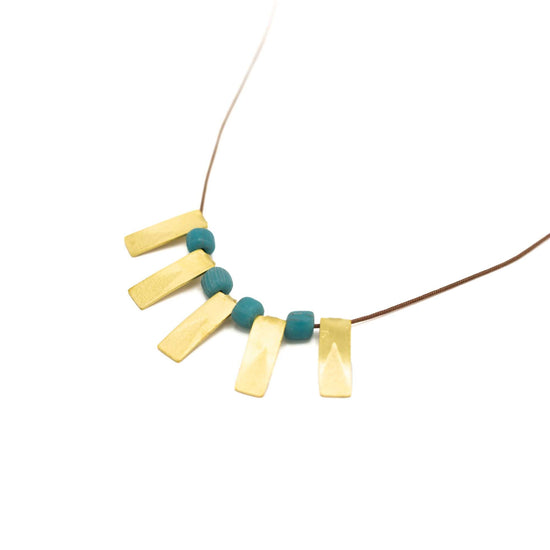 Five brass rectangular pendants with a turquoise glass bead between each. Brown string and presented at an angle against a white background.