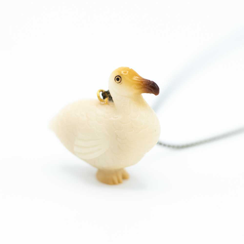 Closer view of tagua carved dodo which is mostly white with some brown on the face and faint yelow on the feet. The chain is out of focus in the background.