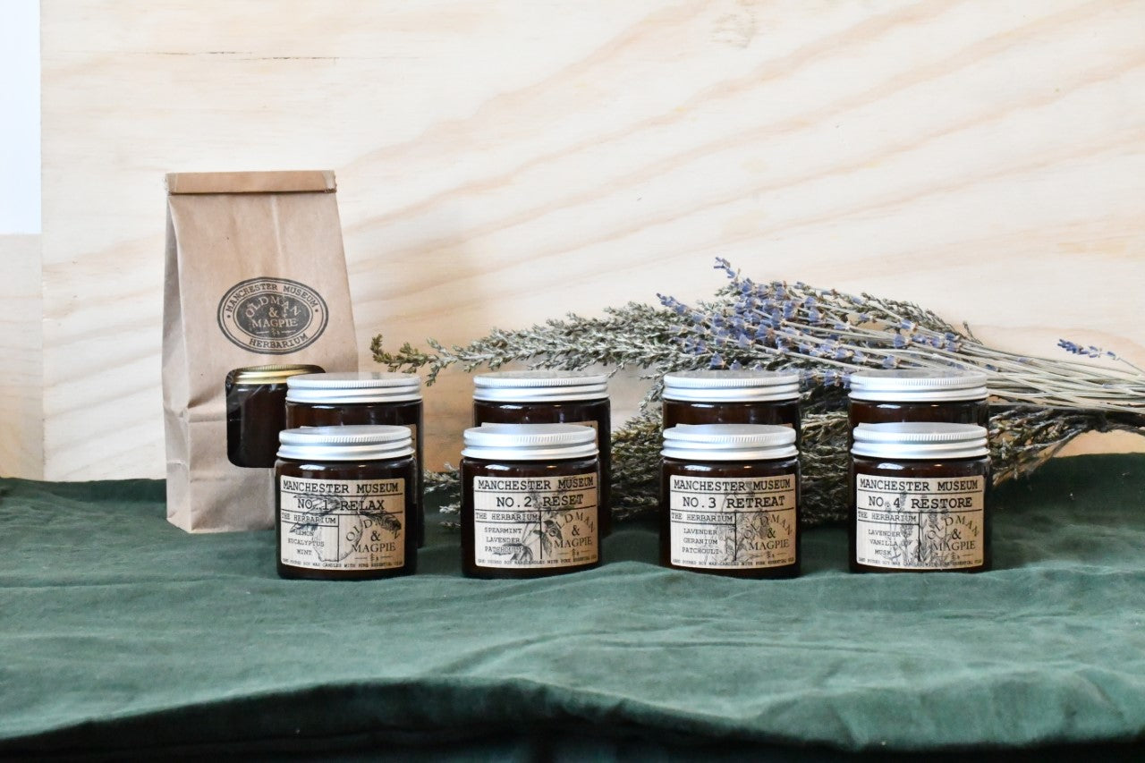 Lifestyle shot with all four scents side by side on a green table cloth. A sheaf of lavender lies in the background.