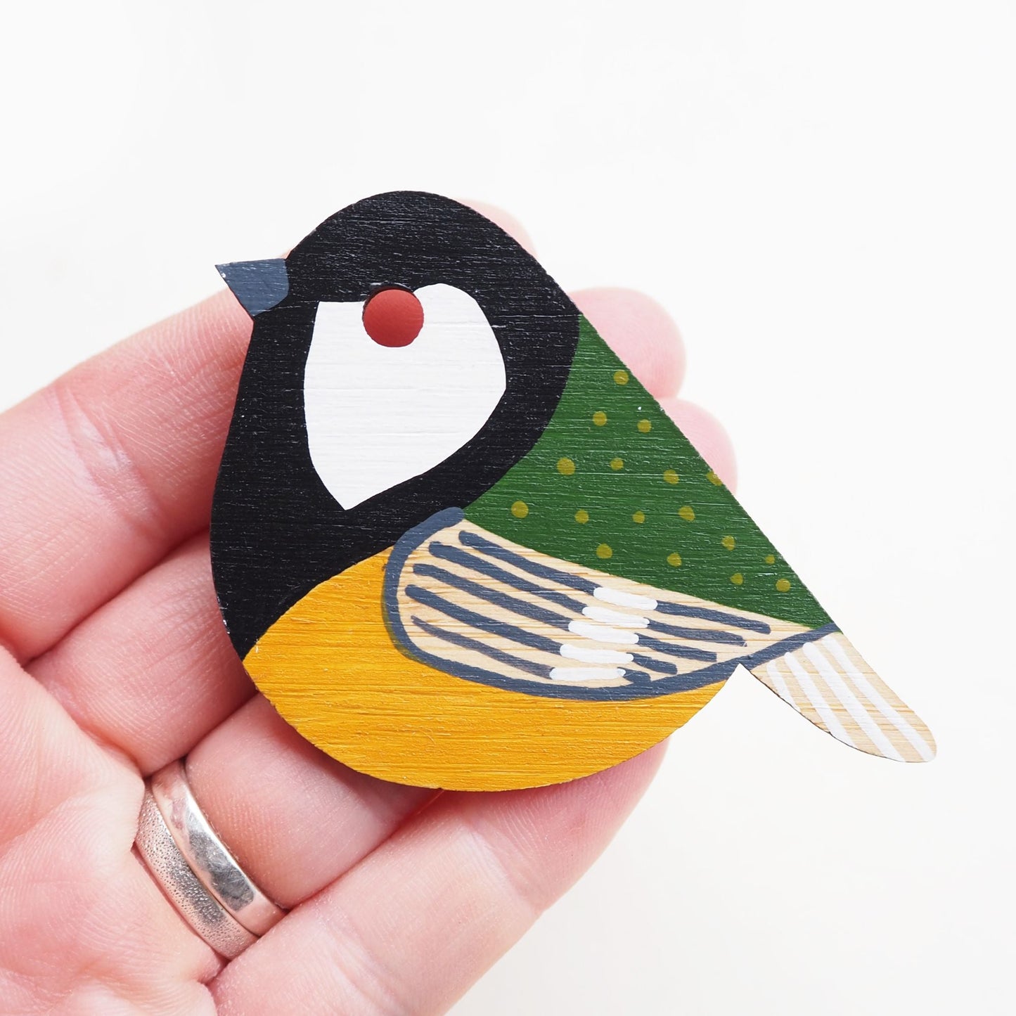 The great tit brooch resting on the tip of four fingers, white backdrop.