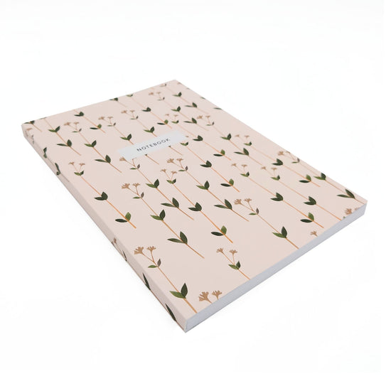 Angled side view of ditsy print notebook in pale pink with many small thin weedy flowers. A white box is one third of the way down form the top with black text reading, notebook.