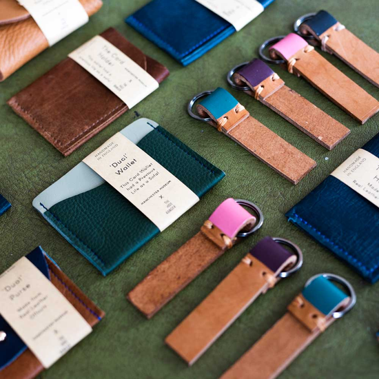 A lifestyle shot with recycled leather keyrings and card wallets in various colours on a green surface.