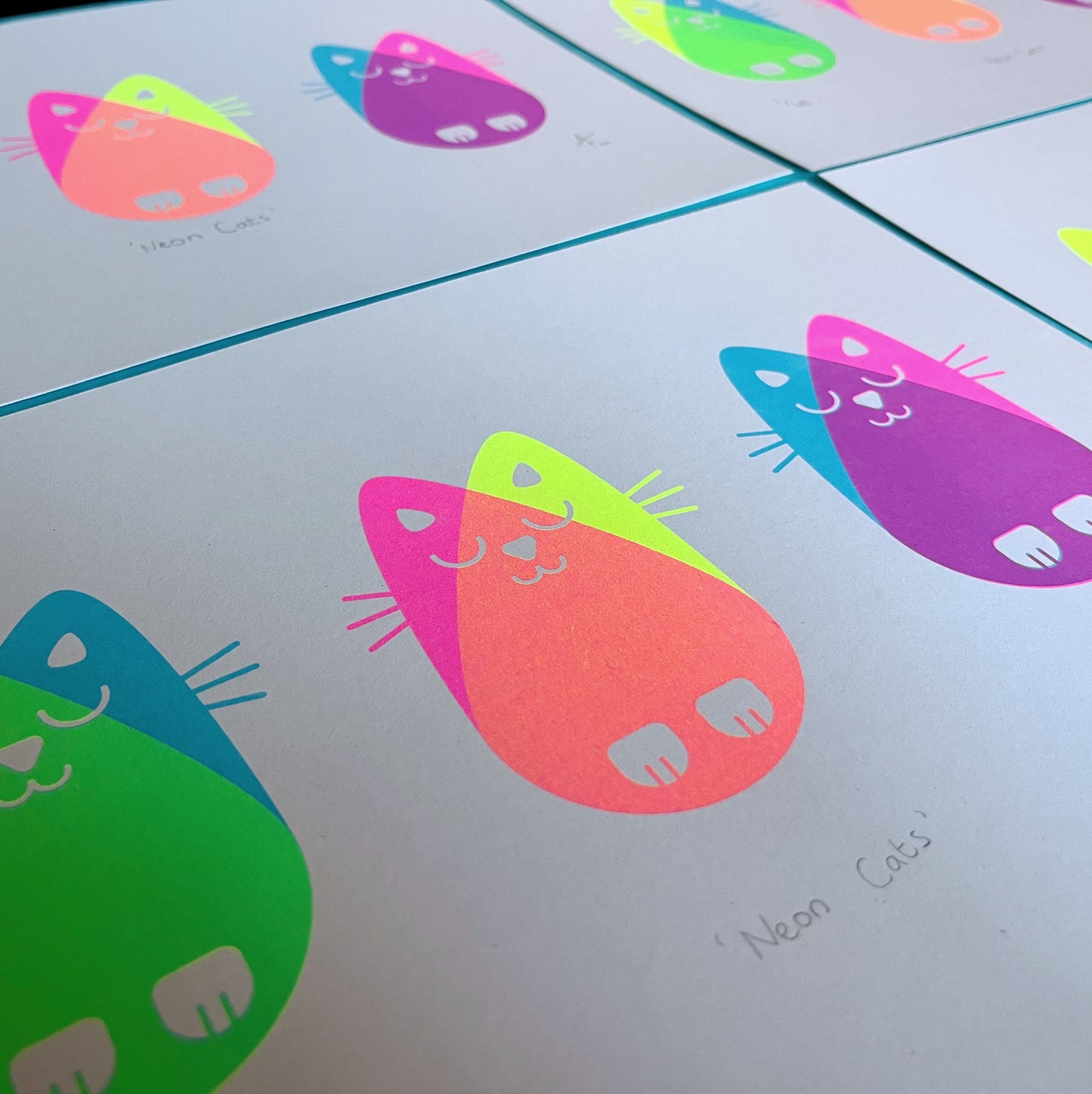 Angled view of several neon cats prints laid out flat.