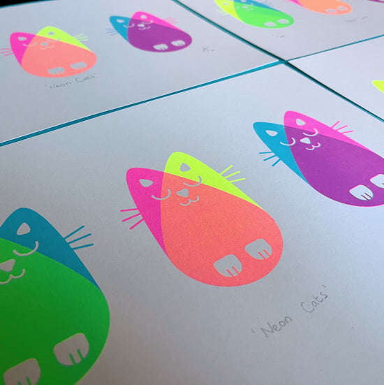 Angled view of several neon cats prints laid out flat.