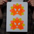 Two colorful Triceratops head illustrations on a white A4 print held by a person wearing a plaid shirt.