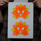 Two colorful Triceratops head illustrations on a white A4 print held by a person wearing a plaid shirt.