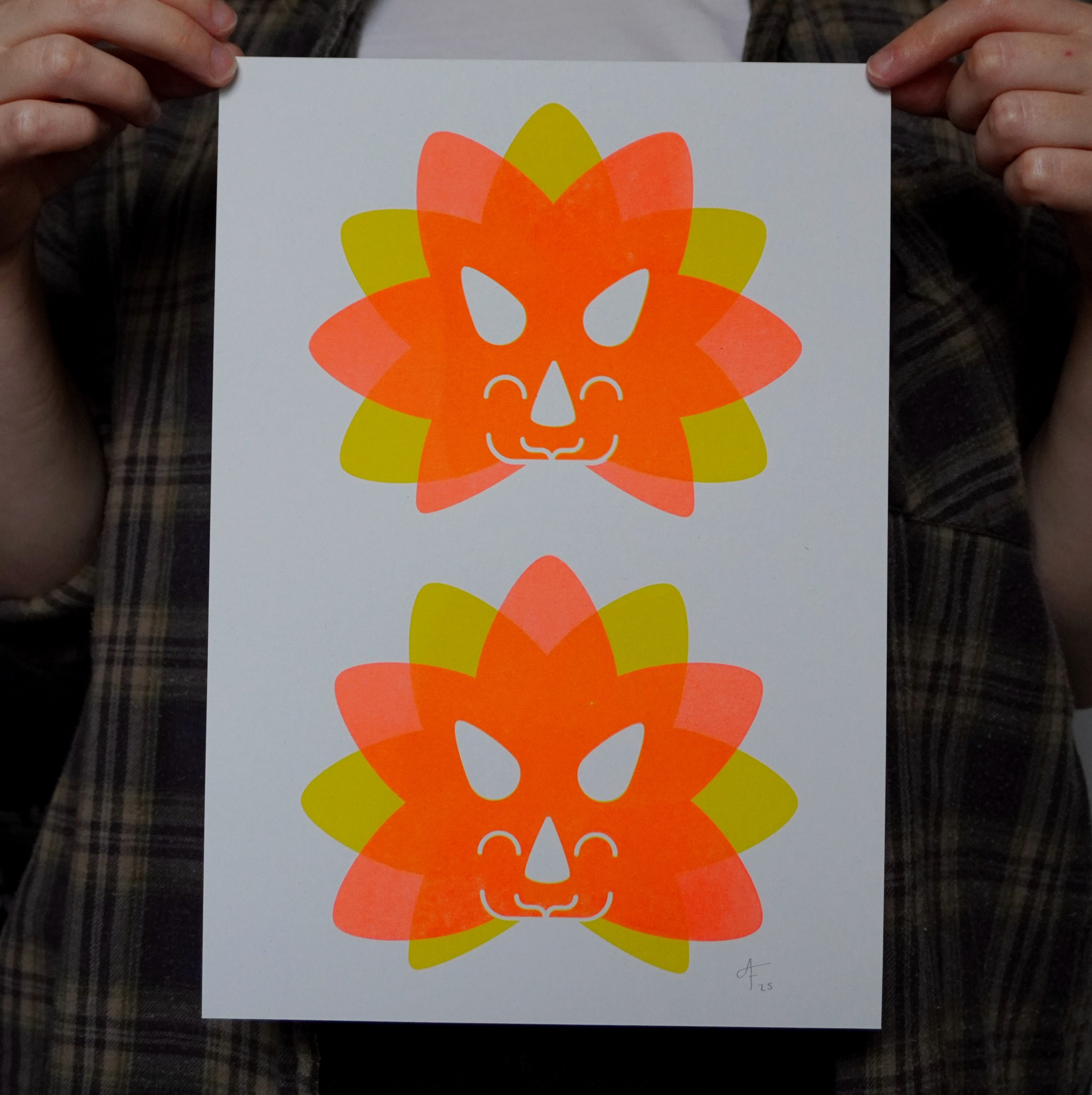 Two colorful Triceratops head illustrations on a white A4 print held by a person wearing a plaid shirt.