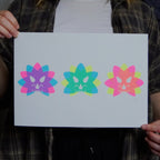 Person holding a white A4 print with 3 colorful Triceratopns head illustrations on.