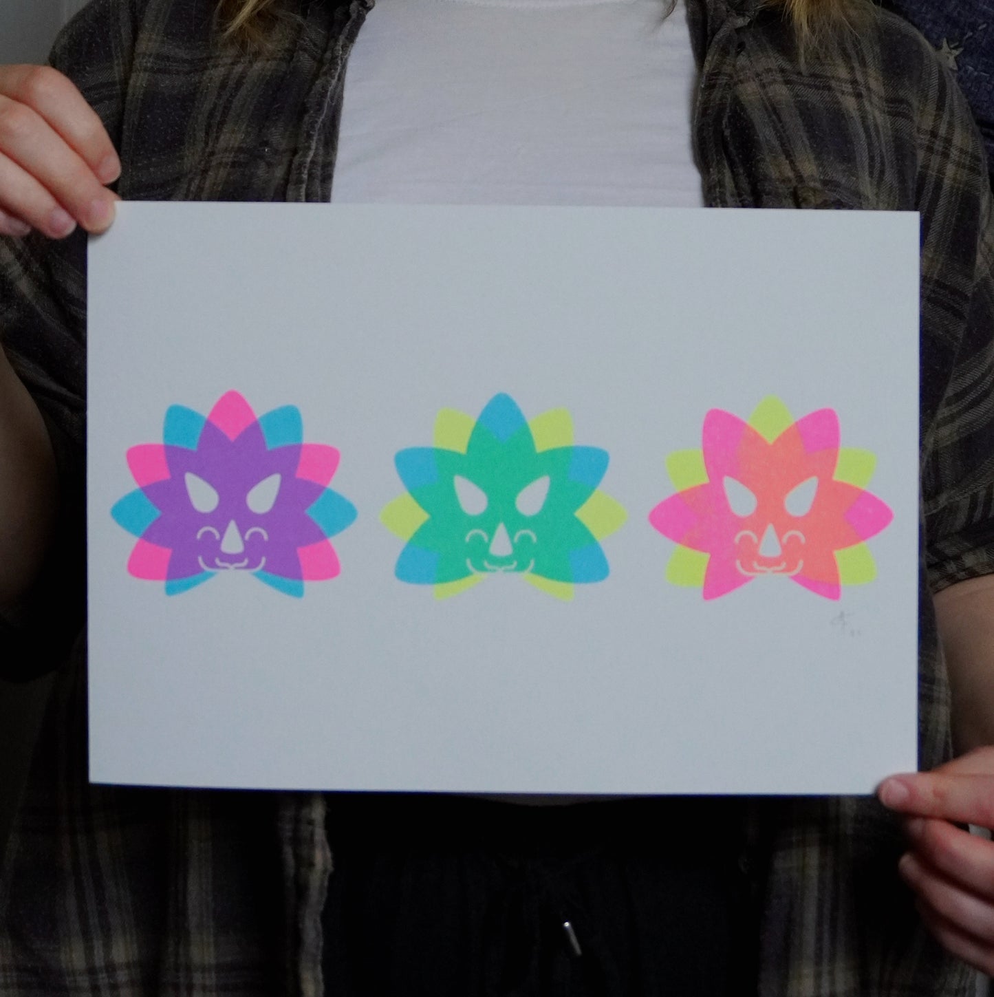Person holding a white A4 print with 3 colorful Triceratopns head illustrations on.