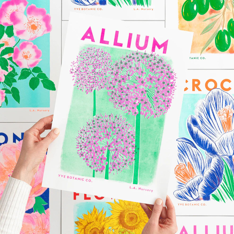 A person holding a risograph print featuring an illustration of an Allium plant