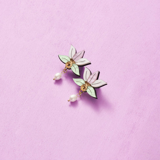 A pair of white pearl drop earrings with delicate floral-shaped charms.