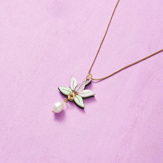 A gold chain necklace with a delicate white pearl pendant and a colorful floral charm.
