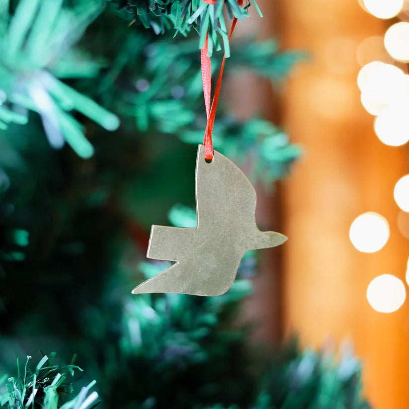 A silver dove-shaped Christmas ornament hanging from a red ribbon on a Christmas tree. The ornament is simple and minimalist.