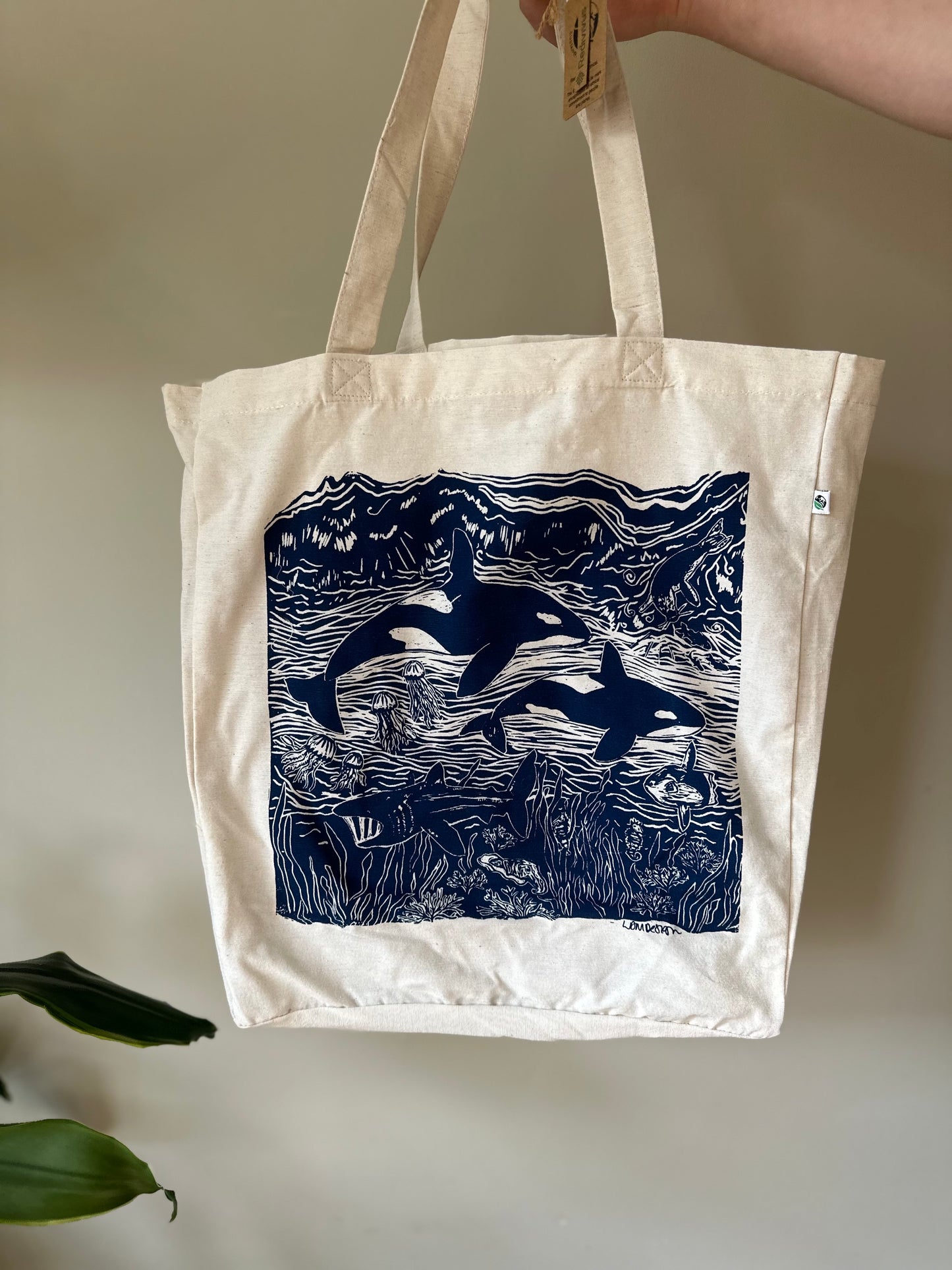 Tote bag with orca whale design held by a hand against a neutral background