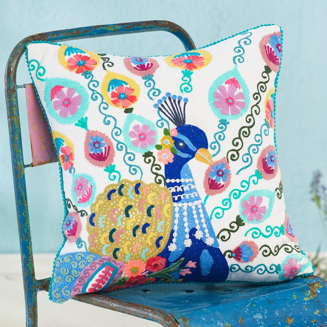 Peacock cusion on a teal painted chair. The cushin has a white background with colourful floral patterns embroidered around a central blue peacock.
