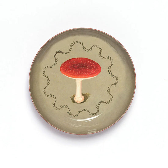 Round enamel tray with a fly agaric mushroom design on a beige background.