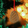 A brass pine cone Christmas ornament hanging from a red ribbon on a Christmas tree. The ornament is simple and minimalist.