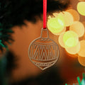 A brass Christmas ornament hanging from a red ribbon on a Christmas tree. The ornament is shaped like a spinning top with intricate geometric patterns.