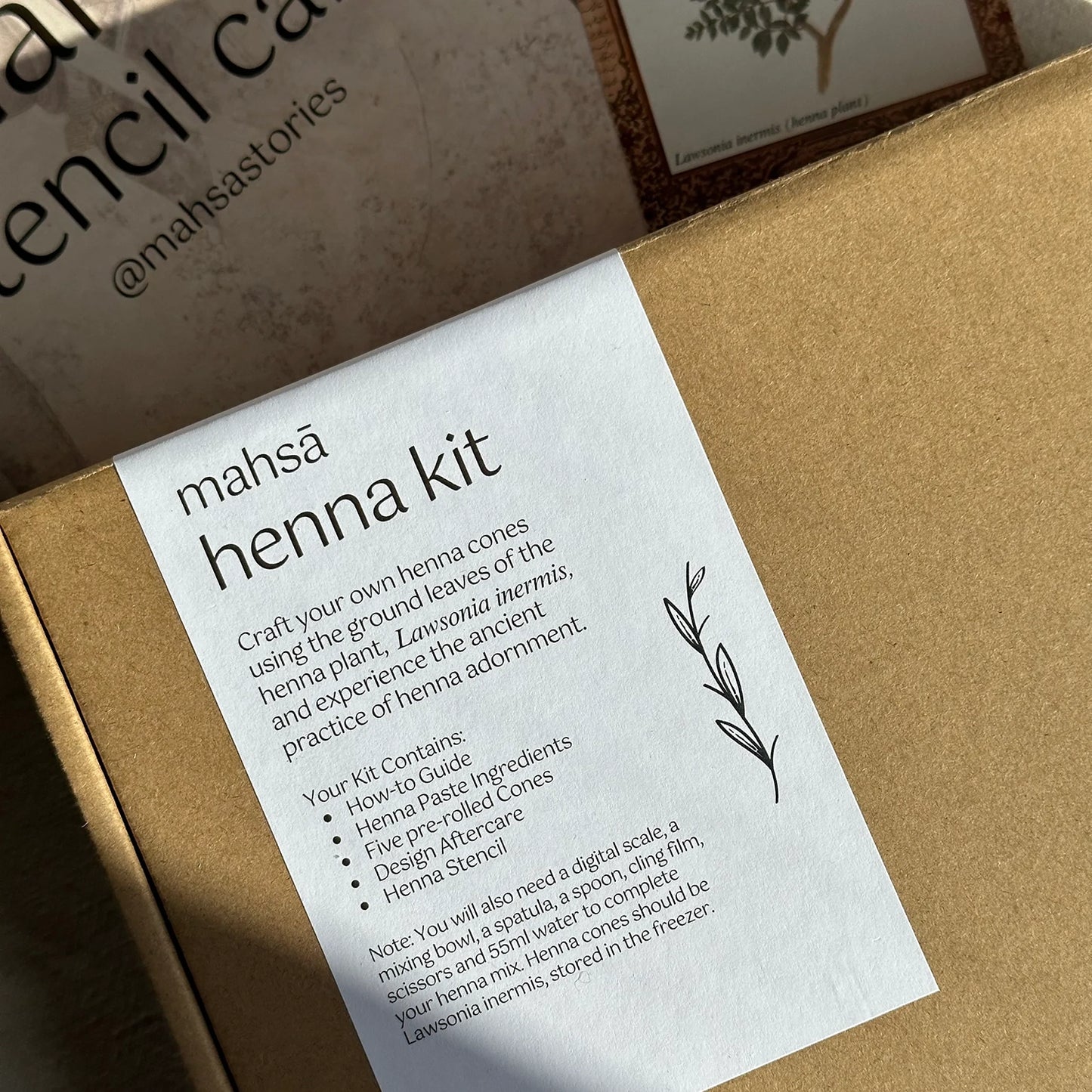 A close-up of a henna kit box. The box has a brown lid with a label that says mahsā henna kit and information about crafting your own henna cones using the ground leaves of the henna plant.