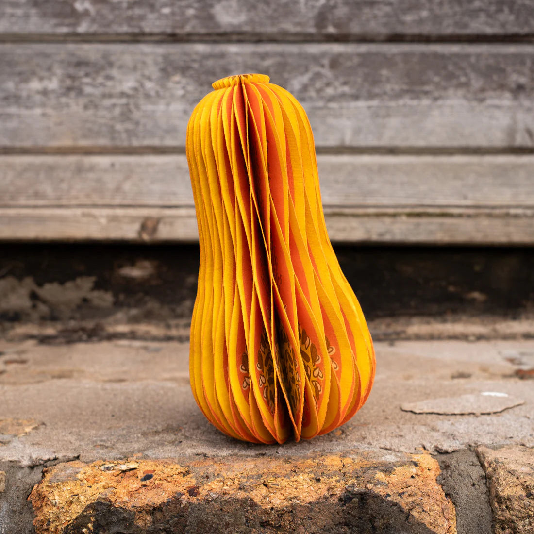 Orange paper sculpture of a squash on a rustic surface.