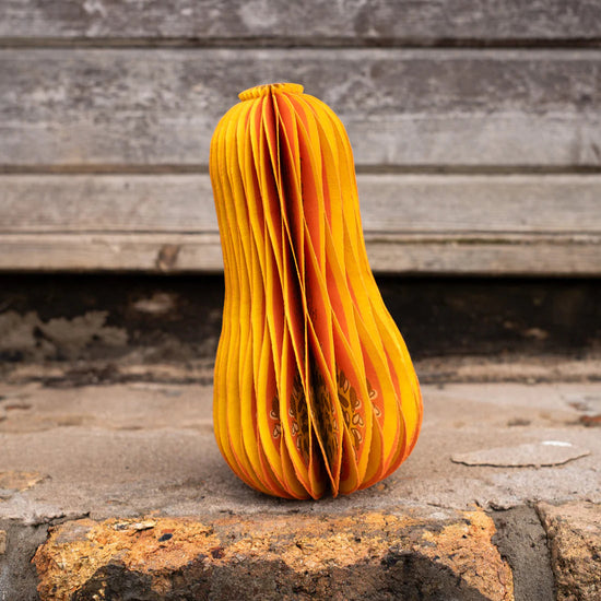 Orange paper sculpture of a squash on a rustic surface.