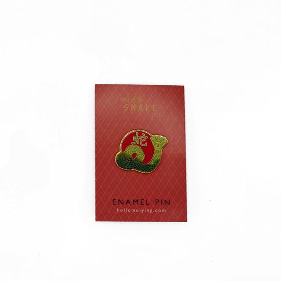 Year of the snake pin on red backing card. The snake pin is gold and red with green accents.