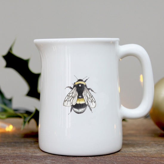 White jug with a bee on it, photographed on a wooden surface