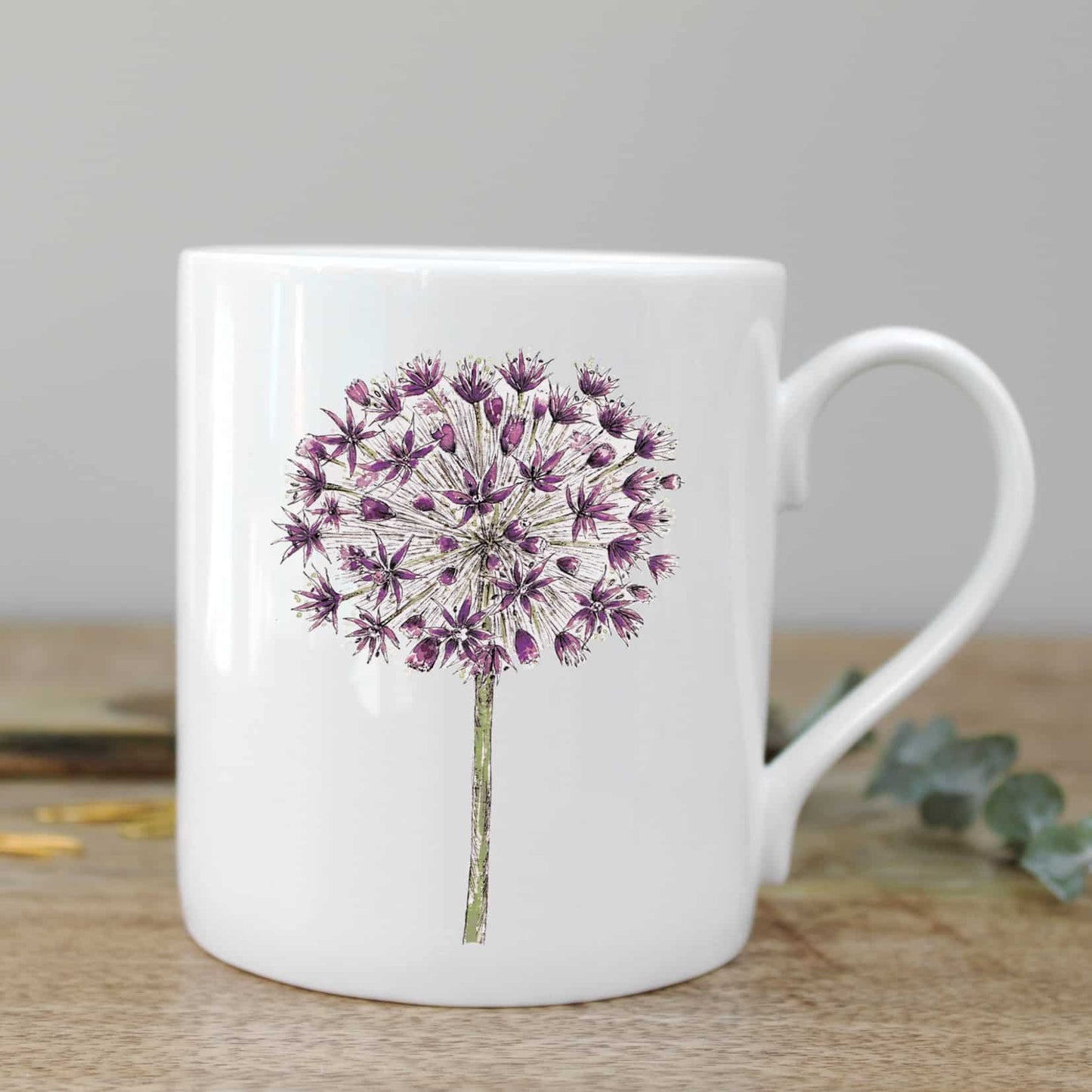 Mug with an illustration of an allium flower. Photographed on a wooden surface. 