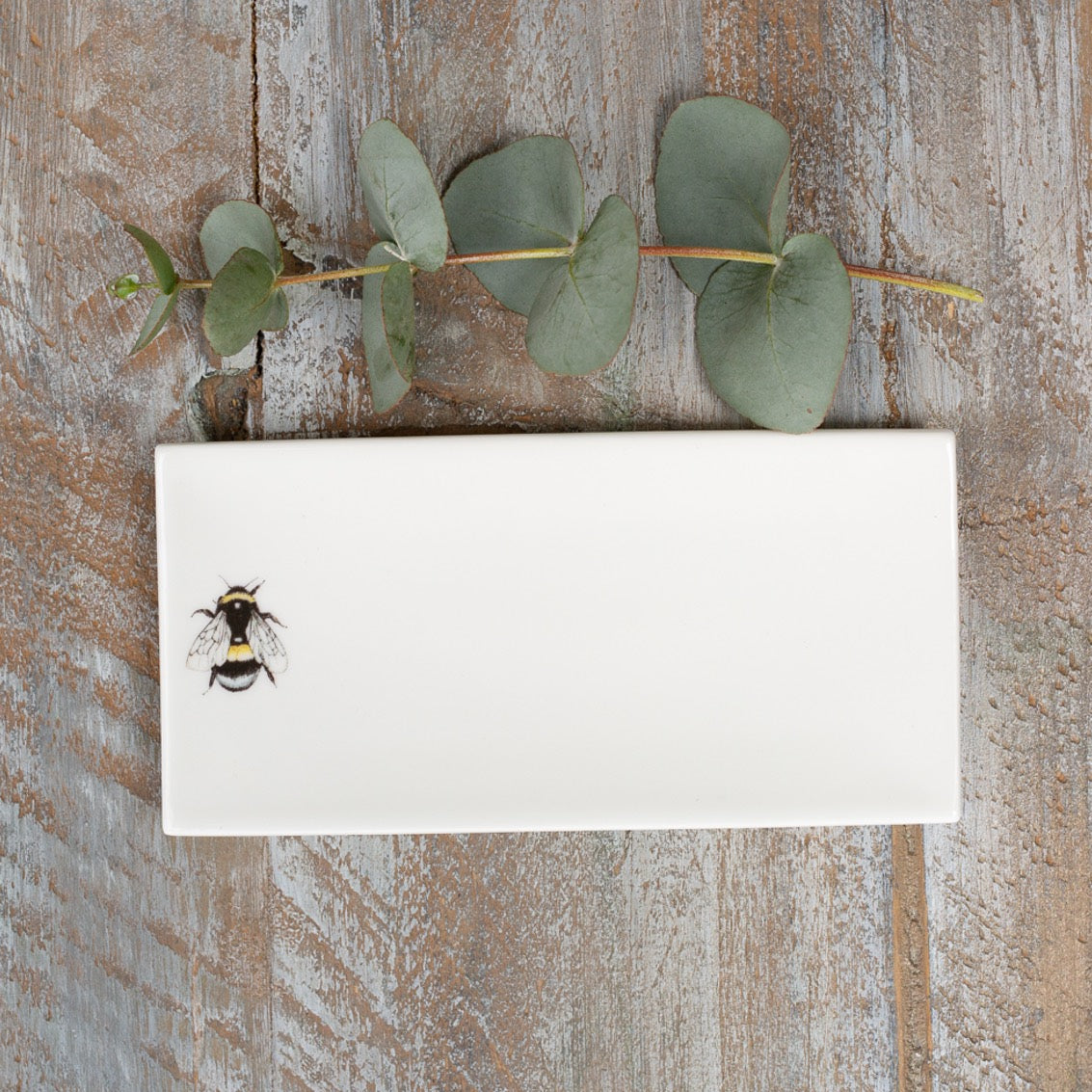 Rectangular soap dish with a picture of a bee on it. Photographed birds-eye-view on a wooden surface