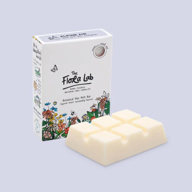 Cream wax melt placed in front of The Flora Lab illustrated packaging. Both photographed in lilac studio setting.