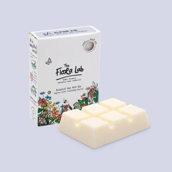 Load image into Gallery viewer, Cream wax melt placed in front of The Flora Lab illustrated packaging. Both photographed in lilac studio setting.
